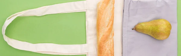 Top view of pear and baguette on eco friendly bags isolated on green, panoramic shot — Stock Photo