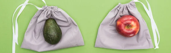 Top view of avocado and apple on eco friendly bags isolated on green, panoramic shot — Stock Photo