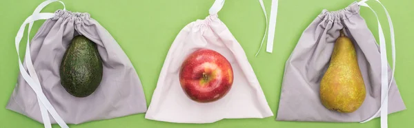Вид зверху на авокадо, грушу та яблуко на екологічно чистих сумках ізольовані на зеленому, панорамному знімку — стокове фото
