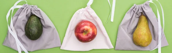 Top view of avocado, pear and apple on eco friendly bags isolated on green, panoramic shot — Stock Photo