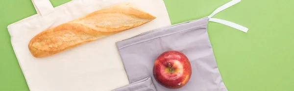 Top view of baguette, apple on eco friendly bags isolated on green, panoramic shot — Stock Photo