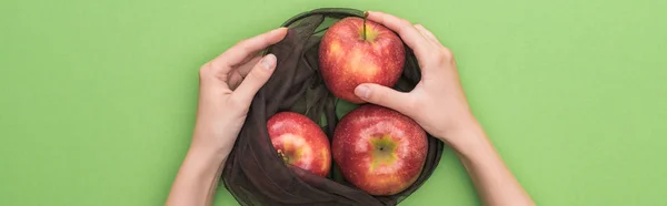 Partial view of woman holding red ripe apples in eco friendly bag isolated on green, panoramic shot — Stock Photo