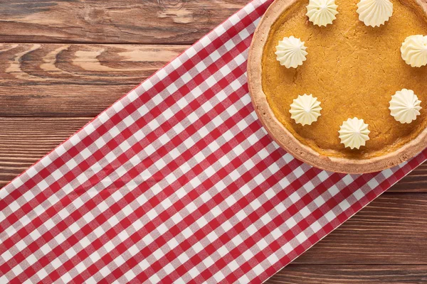 Top view of delicious pumpkin pie with whipped cream on checkered napkin on brown wooden surface — Stock Photo