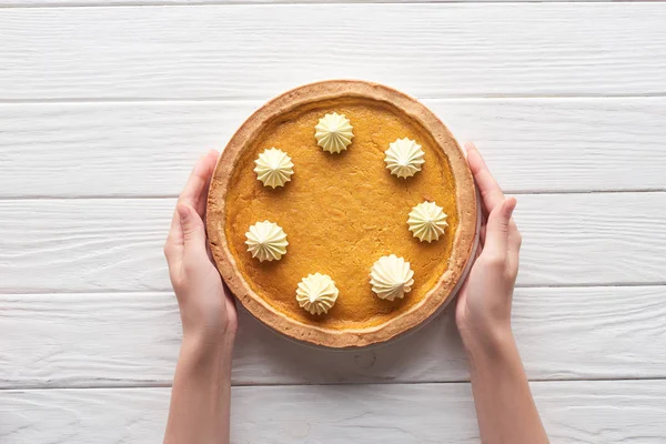 Cropped view of female hands near tasty pumpkin pie with whipped cream on white wooden table — Stock Photo