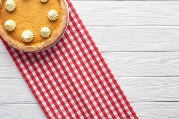 Délicieuse tarte à la citrouille avec crème fouettée et serviette à carreaux sur table en bois blanc — Photo de stock