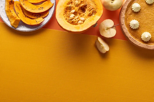 Delicioso pastel de calabaza con crema batida cerca de calabaza al horno en rodajas, manzanas enteras y cortadas, y servilleta texturizada en la superficie naranja - foto de stock