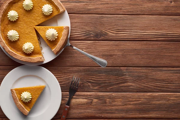 Gustosa torta di zucca con panna montata vicino spatola e forchetta su superficie di legno marrone — Foto stock