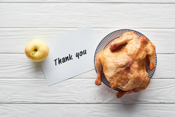 Vista superior de pavo asado, manzana y tarjeta con letras de agradecimiento servidas en mesa de madera blanca - foto de stock