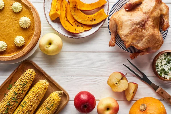 Vista superior de pavo asado, pastel de calabaza y verduras a la parrilla servidas en mesa de madera blanca - foto de stock