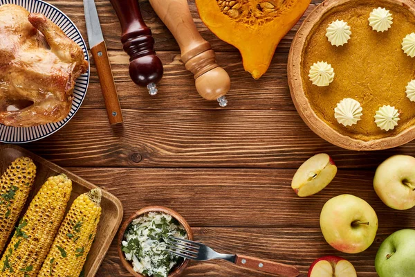 Vista superior de pavo asado, pastel de calabaza y verduras a la parrilla servidas en mesa de madera - foto de stock