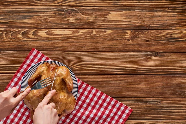 Vista recortada de mujer cortando pavo asado en servilleta a cuadros roja en mesa de madera - foto de stock