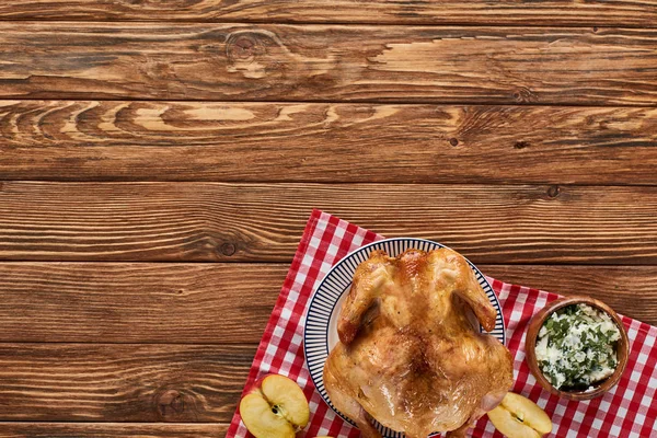 Vue du dessus de la dinde rôtie et de la pomme sur une serviette à carreaux rouge sur une table en bois — Photo de stock