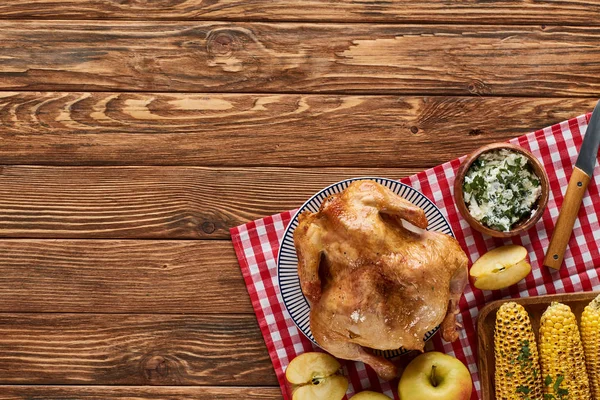 Vue du dessus de la dinde rôtie, du maïs grillé et des pommes sur une serviette à carreaux rouge sur une table en bois — Photo de stock