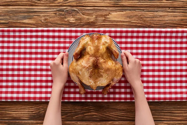 Vista recortada de la mujer sosteniendo pavo asado en servilleta a cuadros rojo en la mesa de madera - foto de stock