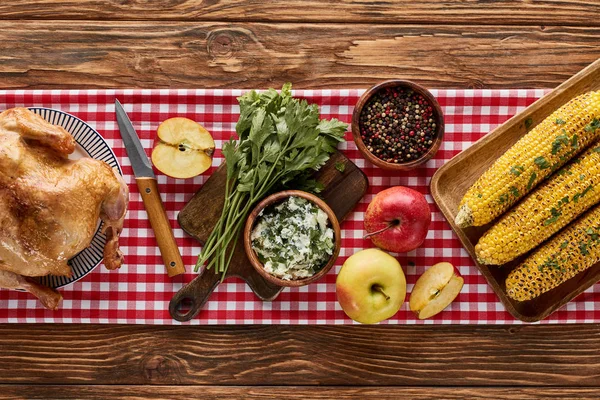 Vista superior de peru assado, milho grelhado e maçãs com salsa e pimenta servida em mesa de madeira com guardanapo vermelho — Fotografia de Stock