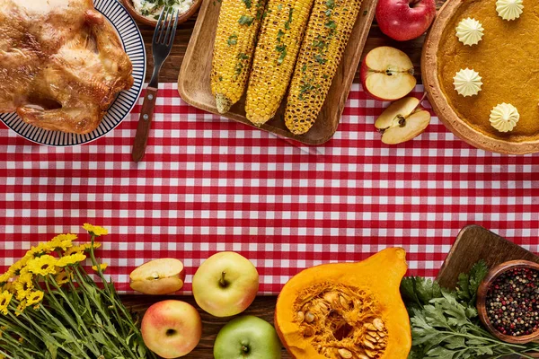 Vista superior de pavo asado, pastel de calabaza y verduras a la parrilla servidas en mesa de madera con servilleta a cuadros roja - foto de stock