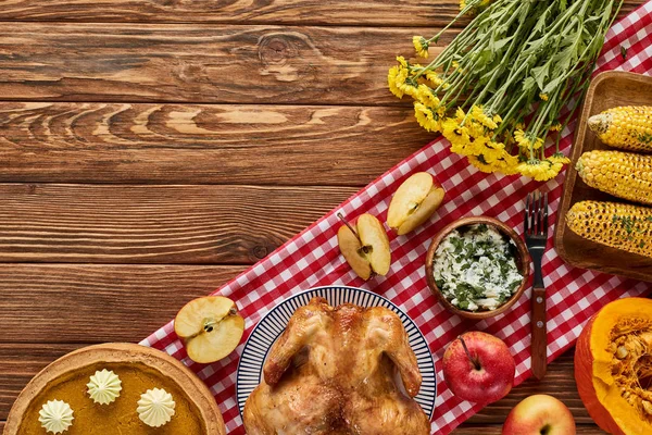 Vue de dessus de dinde rôtie, tarte à la citrouille et légumes grillés servis sur une table en bois avec des fleurs et une serviette à carreaux — Photo de stock