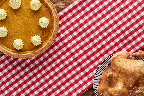 Vue de dessus de délicieuse tarte à la citrouille et dinde rôtie servie sur une serviette à carreaux rustique sur une table en bois — Photo de stock