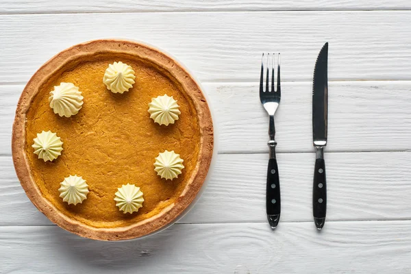 Vista superior de pastel de calabaza y cubiertos servidos en mesa de madera blanca - foto de stock