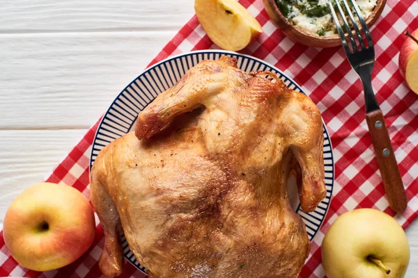 Vue de dessus de dinde rôtie, pommes servies sur table en bois blanc avec serviette à carreaux rouge — Photo de stock