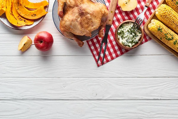 Top view of roasted turkey, pumpkin pie and grilled corn served on white wooden table with red plaid napkin — Stock Photo