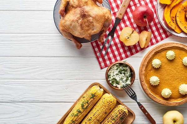 Blick von oben auf gebratenen Truthahn, Kürbiskuchen und gegrilltes Gemüse, serviert auf weißem Holztisch mit rot karierter Serviette — Stockfoto