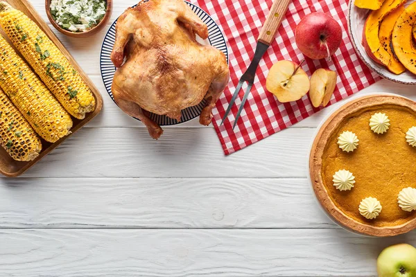 Vista superior de pavo asado, pastel de calabaza y verduras a la parrilla servidas en mesa de madera blanca con servilleta a cuadros roja - foto de stock