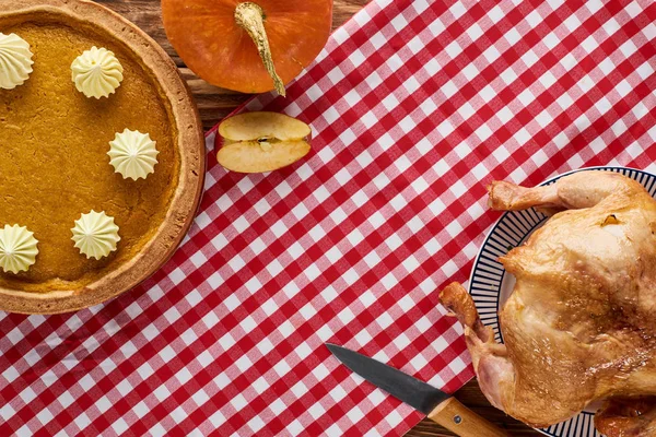 Vue du dessus de la dinde rôtie, tarte à la citrouille et citrouille servie sur une serviette rouge à carreaux sur une table en bois — Photo de stock