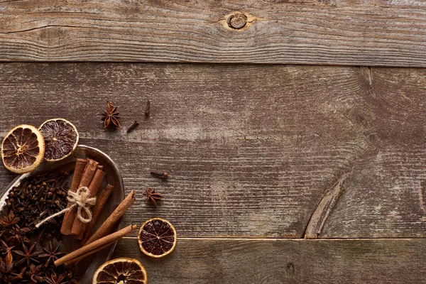 Vista superior de palitos de canela, anís y cítricos secos sobre una mesa rústica de madera - foto de stock