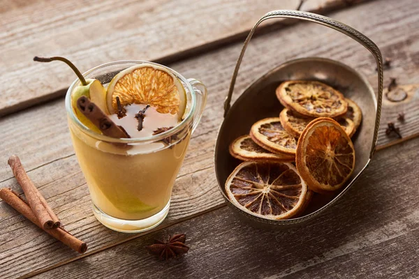 Traditioneller Birnen-Glühwein mit Gewürzen im Glas neben getrockneten Zitrusfrüchten auf rustikalem Holztisch — Stockfoto