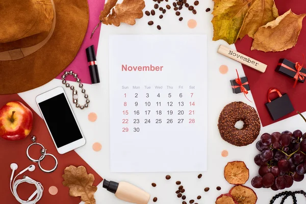 Smartphone, hat, dry leaves, fresh and dry apples, grapes, donut, cosmetics, coffee grains and wooden block with november inscription isolated on white — Stock Photo