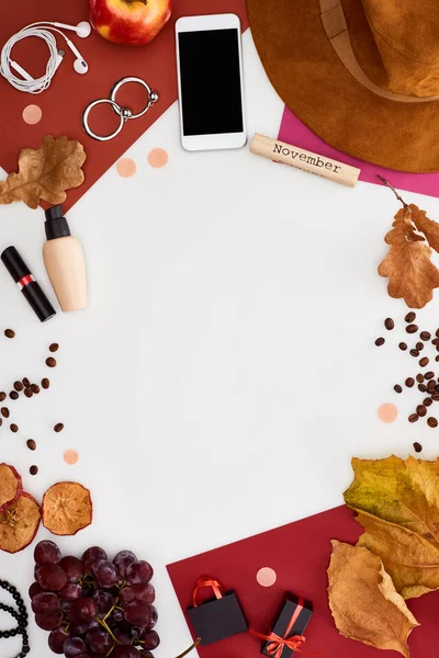 Smartphone, chapeau, feuilles sèches, pommes fraîches et sèches, raisins, beigne, cosmétiques, grains de café et bloc de bois avec inscription de novembre isolé sur blanc — Photo de stock