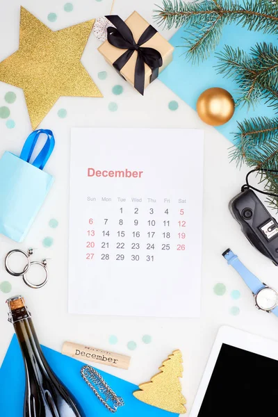 Página del calendario de diciembre cerca de la cámara digital, botella de champán, adornos de Navidad, rama de abeto, reloj de pulsera, papel azul aislado en blanco - foto de stock