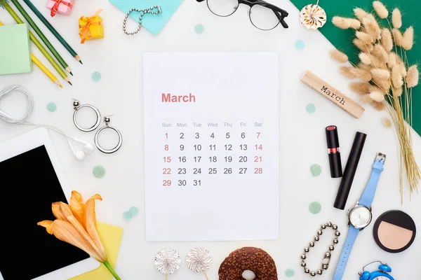 Página calendario de marzo, tableta digital, flor de lirio, espiguillas, cosméticos, dona, lápices, cajas de regalo, reloj de pulsera, reloj despertador de juguete, bloque con inscripción de marzo aislado en blanco — Stock Photo
