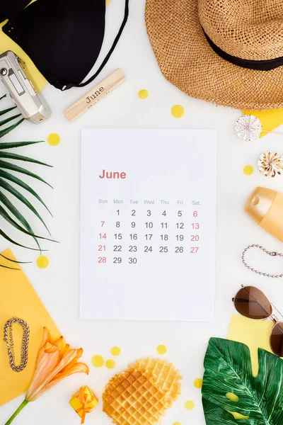 June calendar page, wooden block with june inscription, straw hat, digital camera, lily flower, green leaves, sunglasses, sunscreen, waffles, bikini bra isolated on white — Stock Photo