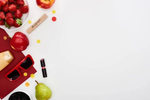 Morango fresco, maçãs, pêra, óculos de sol, cosméticos, papel vermelho, bloco de madeira com inscrição agosto isolado em branco — Fotografia de Stock