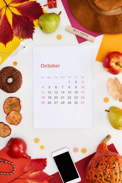 Página del calendario de octubre, sombrero, teléfono inteligente, frutas, calabaza, hojas secas, papeles multicolores, bloque de madera con inscripción de octubre aislado en blanco - foto de stock