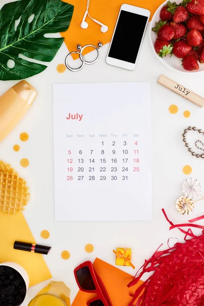 Página de calendário julho, bloco de madeira com inscrição julho, morango fresco, smartphone, chapéu de palha, óculos de sol, cosméticos, folha verde, waffles, pirulitos isolados em branco — Fotografia de Stock