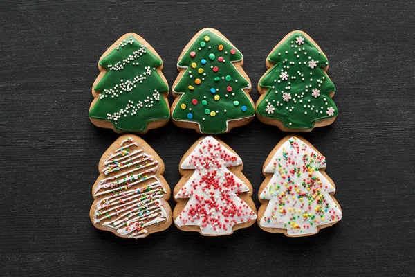 Flat lay with delicious glazed Christmas tree cookies on black background — Stock Photo