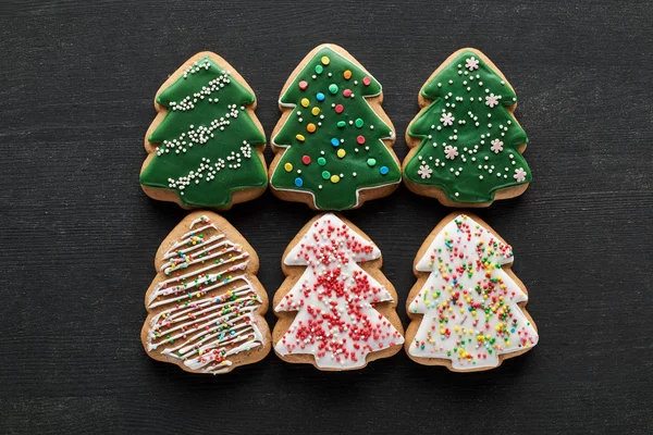 Flache Lage mit leckeren glasierten Christbaumkeksen auf schwarzem Hintergrund — Stockfoto