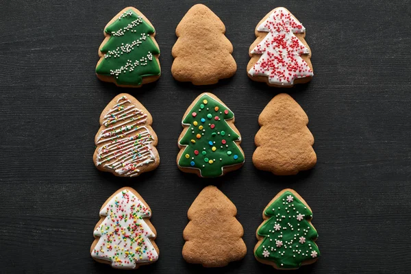 Flat lay with delicious glazed Christmas tree cookies on black background — Stock Photo