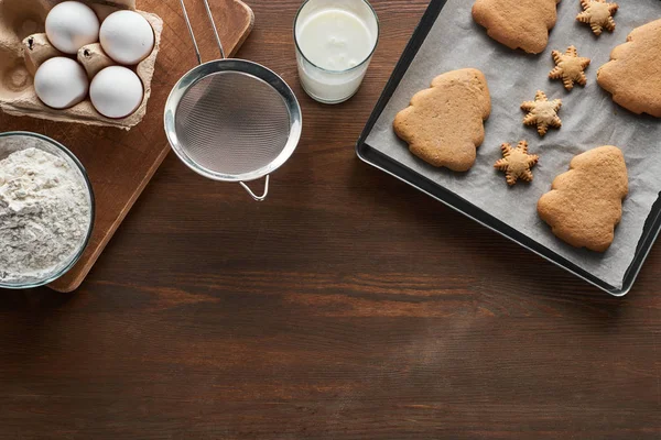 Vista superior de biscoitos de Natal na bandeja do forno perto de ingredientes na mesa de madeira — Fotografia de Stock