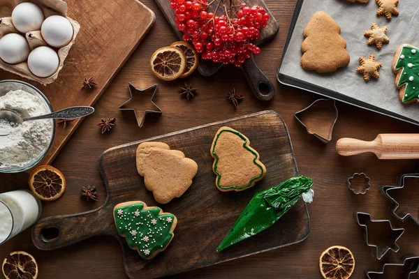 Top view of glazed Christmas cookies near ingredients, dough molds and viburnum on wooden table — Stock Photo