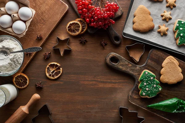 Vista superior de biscoitos de Natal envidraçados perto de ingredientes, moldes de massa e viburnum na mesa de madeira — Fotografia de Stock