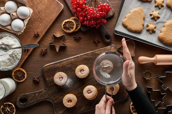 Cropped view of woman sieving sugar powder on Christmas cookies at wooden table — Stock Photo