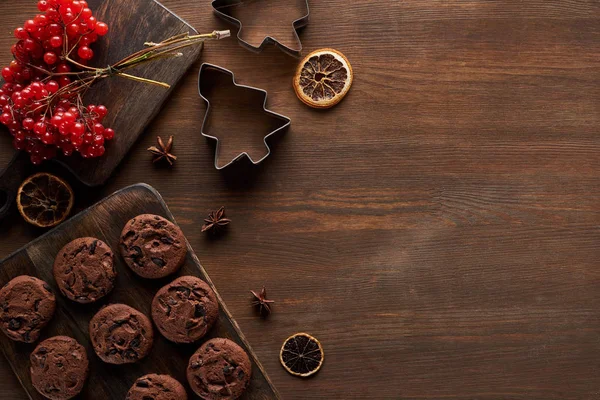 Top view of chocolate cookies near Christmas dough molds, viburnum and spices on wooden table — Stock Photo