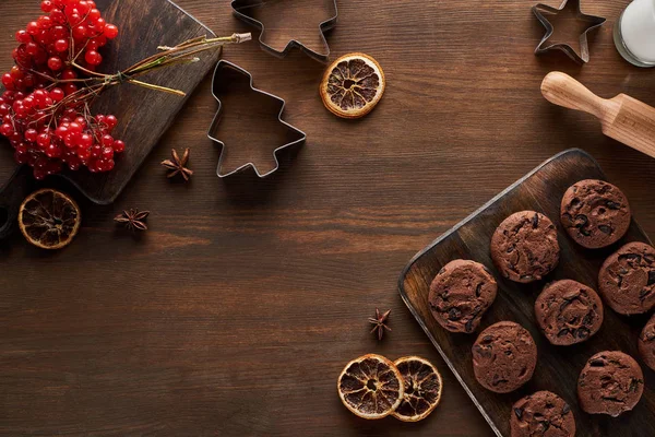 Vista superior de biscoitos de chocolate perto de moldes de massa de Natal, viburnum e especiarias na mesa de madeira — Fotografia de Stock