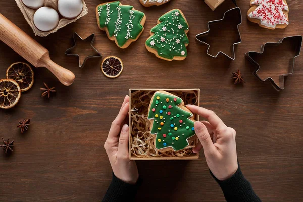 Cropped view of woman putting Christmas tree cookie in gift box on wooden table — Stock Photo