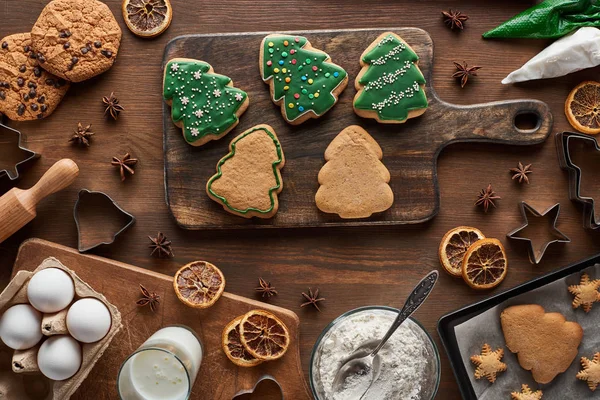 Vista superior de biscoitos de árvore de Natal perto de ingredientes em mesa de madeira — Fotografia de Stock