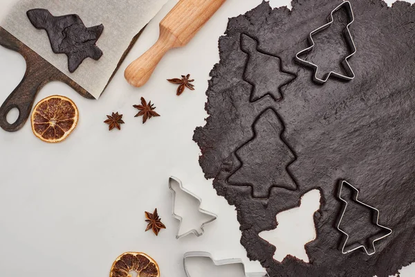 Vue du dessus de la pâte crue pour biscuits de Noël au chocolat sur fond blanc près de l'anis, fruits secs et rouleau à pâtisserie — Photo de stock